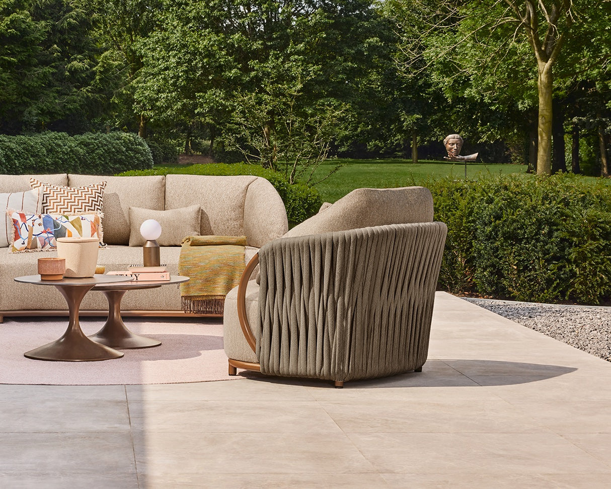 Outdoor patio setting with beige sofa, armchair, and coffee table in a garden.