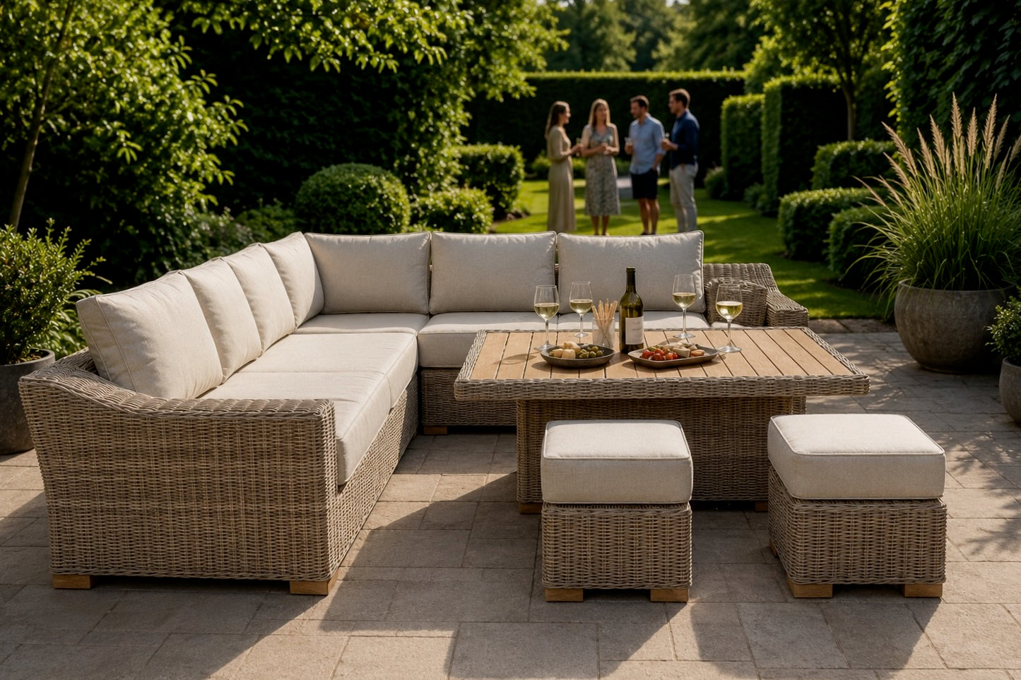Outdoor patio furniture set in a garden, featuring a wicker sectional sofa with cream cushions, a matching rectangular coffee table, and two ottomans, with people dining in the background.