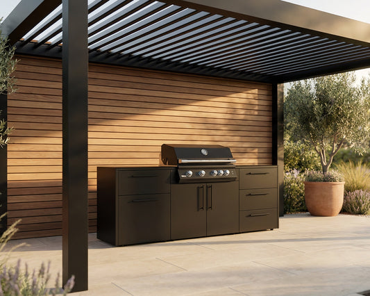 A black outdoor kitchen island set with a built-in gas grill, positioned under a modern black pergola with a wood-paneled wall and potted plants in the background.